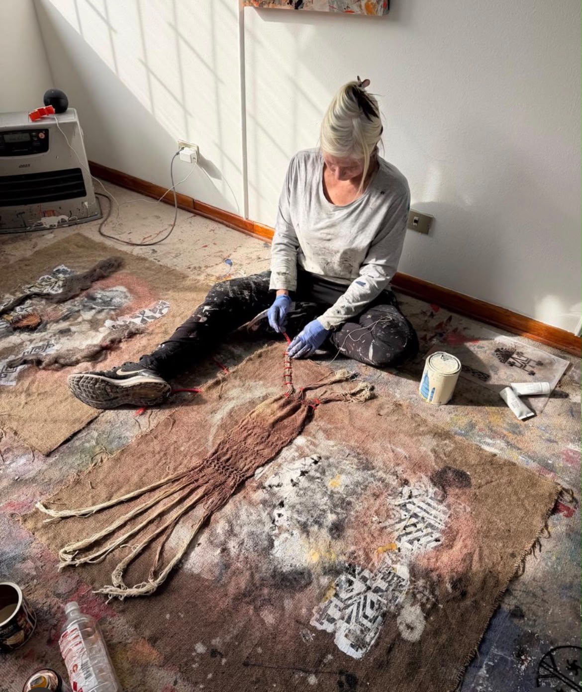 Marcela Krause trabajando arrodillada sobre una pieza textil intervenida con hilo y pigmento en su taller